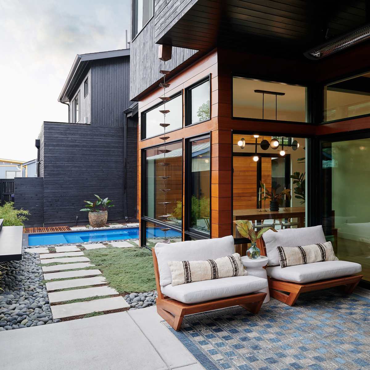 A modern backyard with two chairs facing a pool, surrounded by a landscaped area with stones and grassy patches.