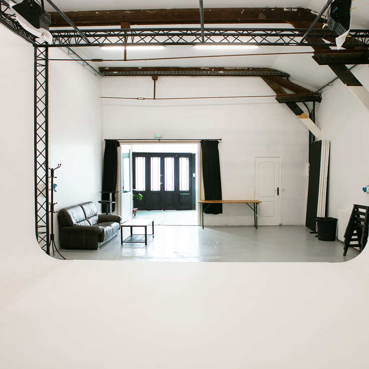 A spacious, minimalist studio with a leather sofa, a wooden table, and large windows framed by black curtains.
