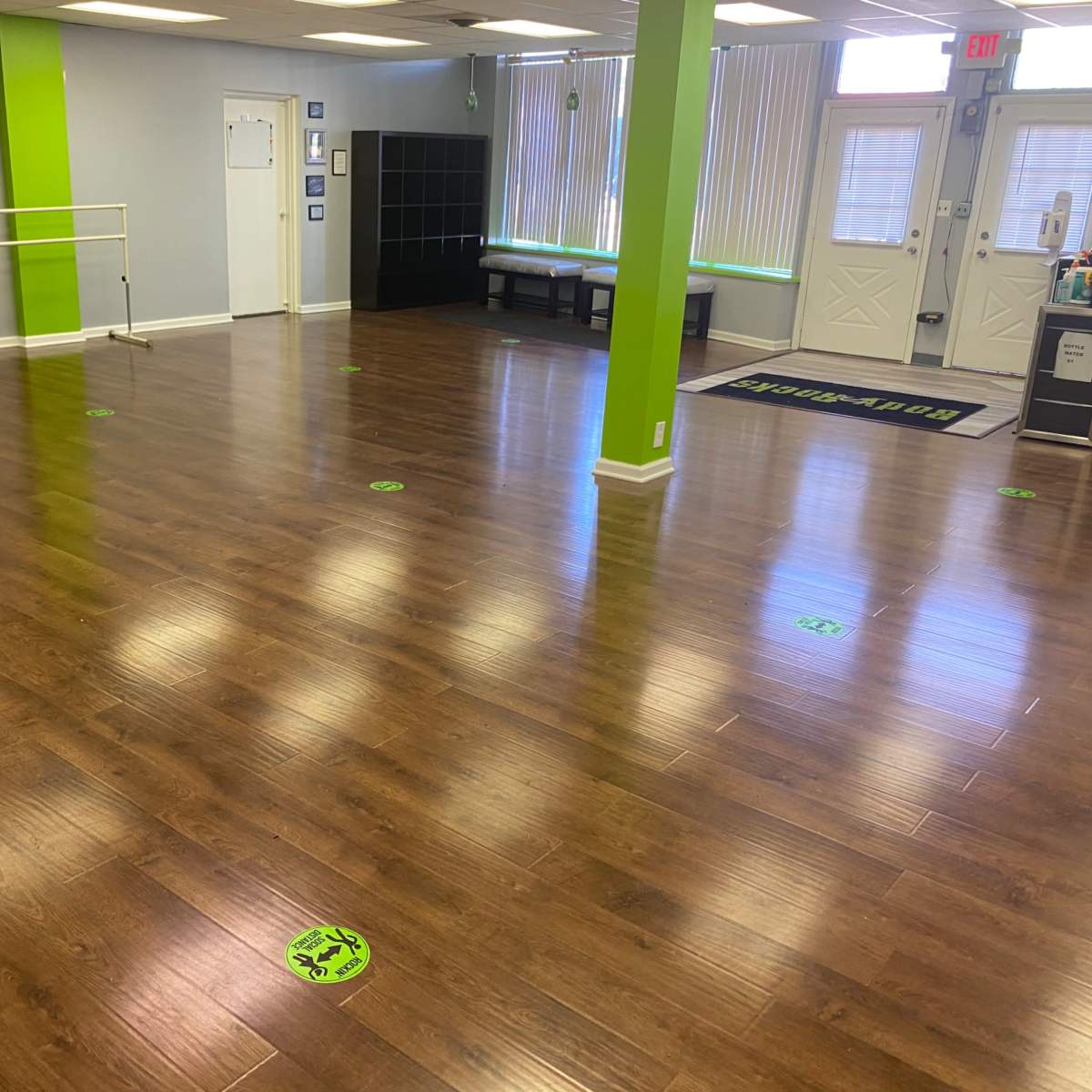 A spacious, empty dance studio with a wooden floor and green markings on the ground for social distancing.