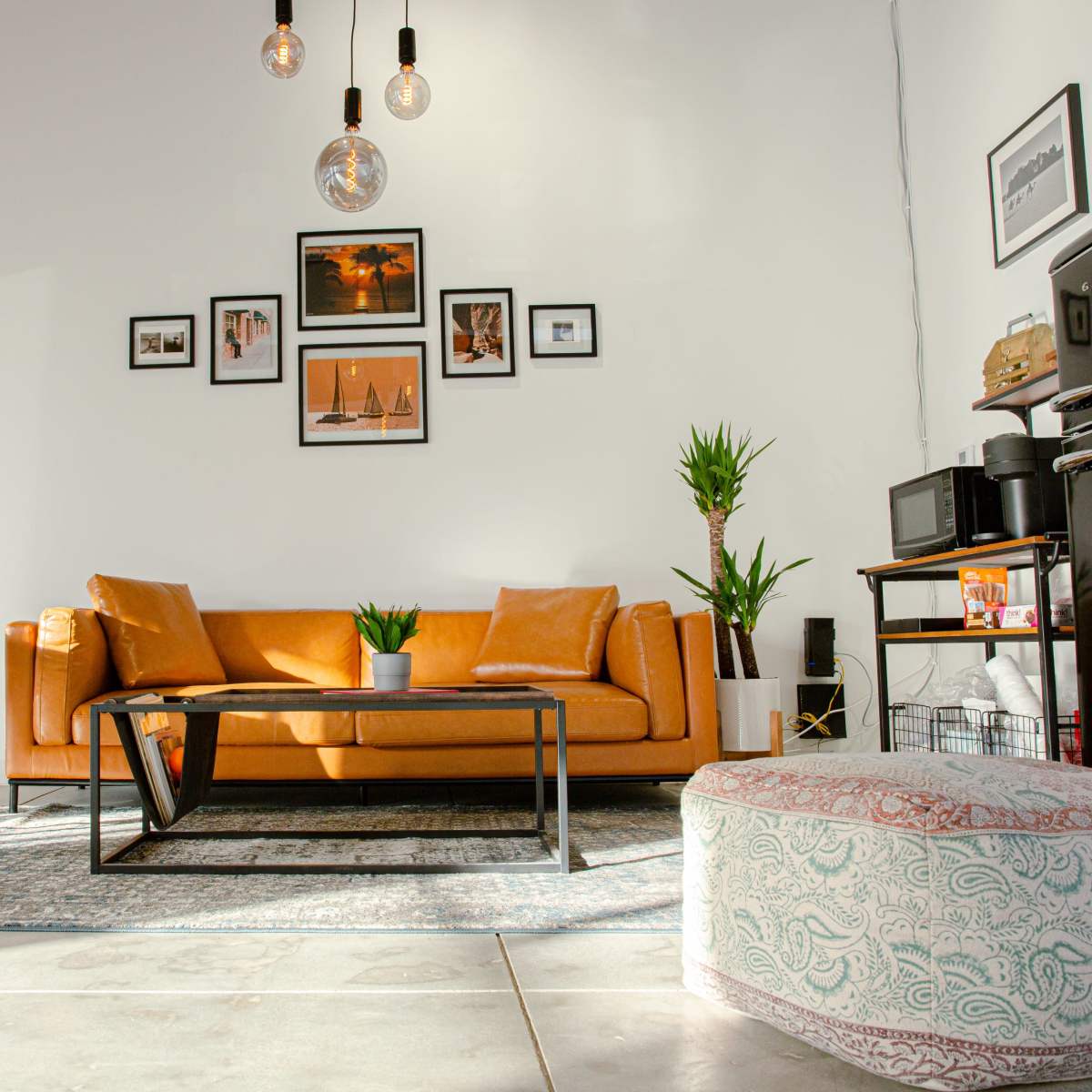 The scene depicts a modern living room with a brown sofa, a coffee table, various framed pictures on the wall, and plants, illuminated by pendant lights.