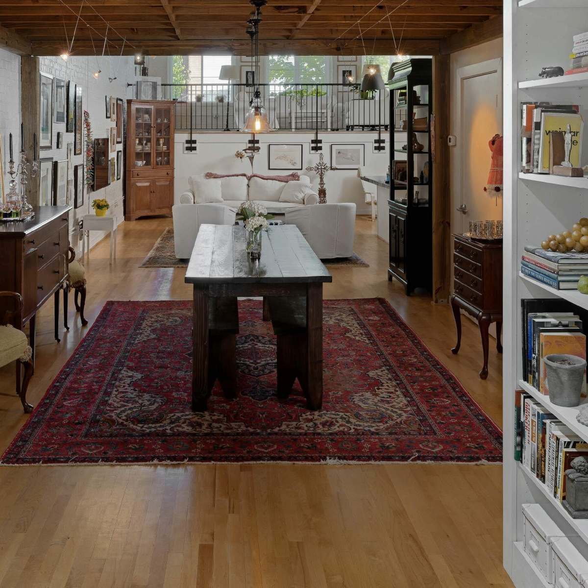 A spacious, open-concept living area with wooden beams, a large rug, and a seating area featuring white sofas.