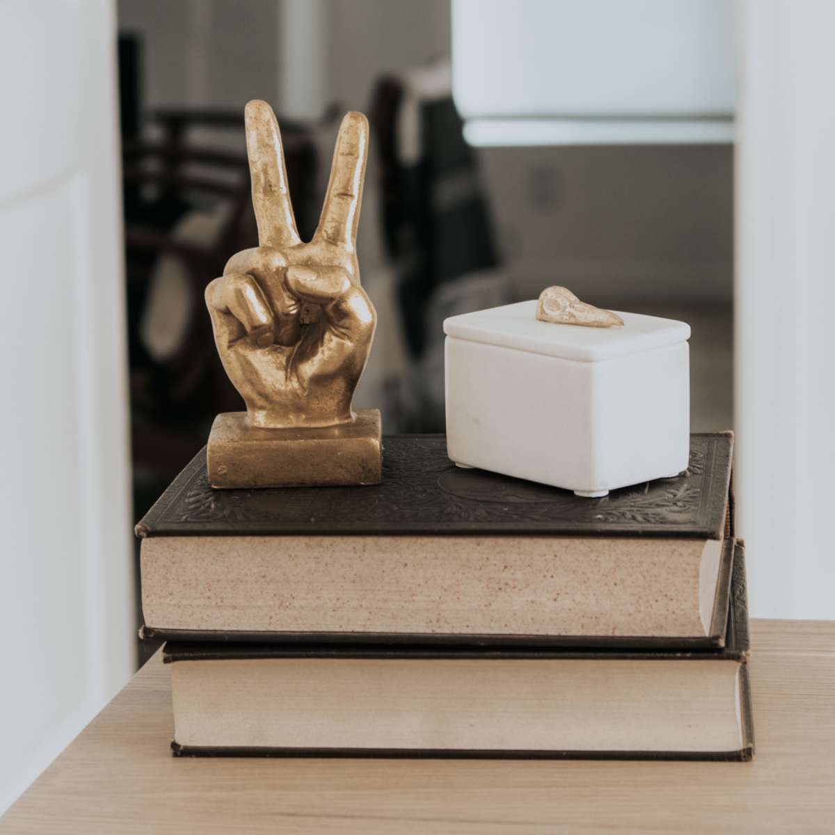 A gold hand figurine making a peace sign rests on top of stacked books next to a small white container.