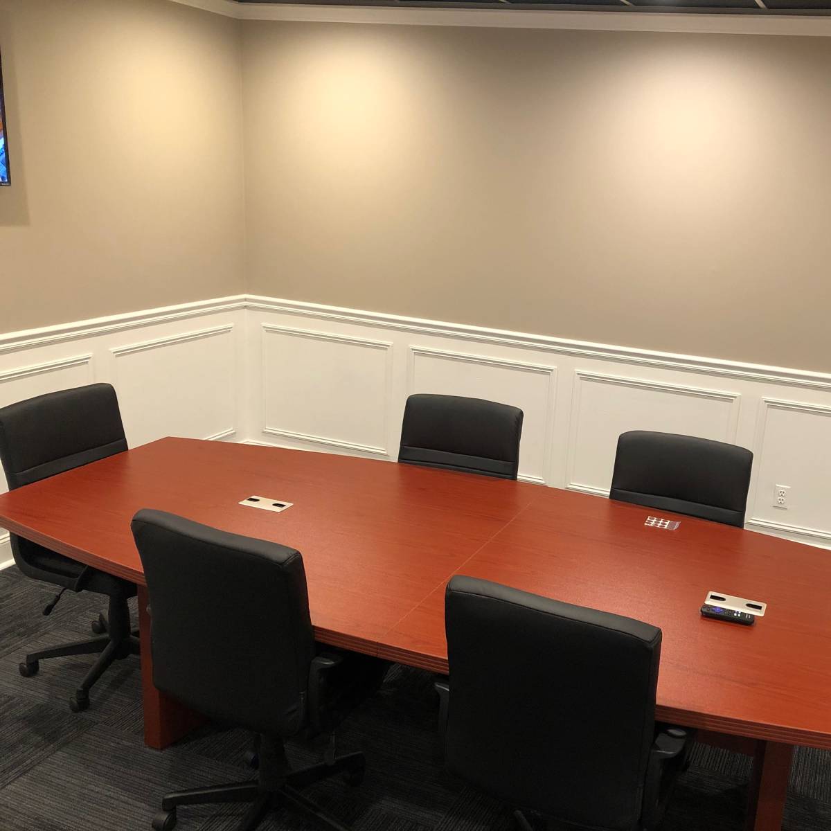 A long, oval wooden conference table is surrounded by six black office chairs in a well-lit meeting room.