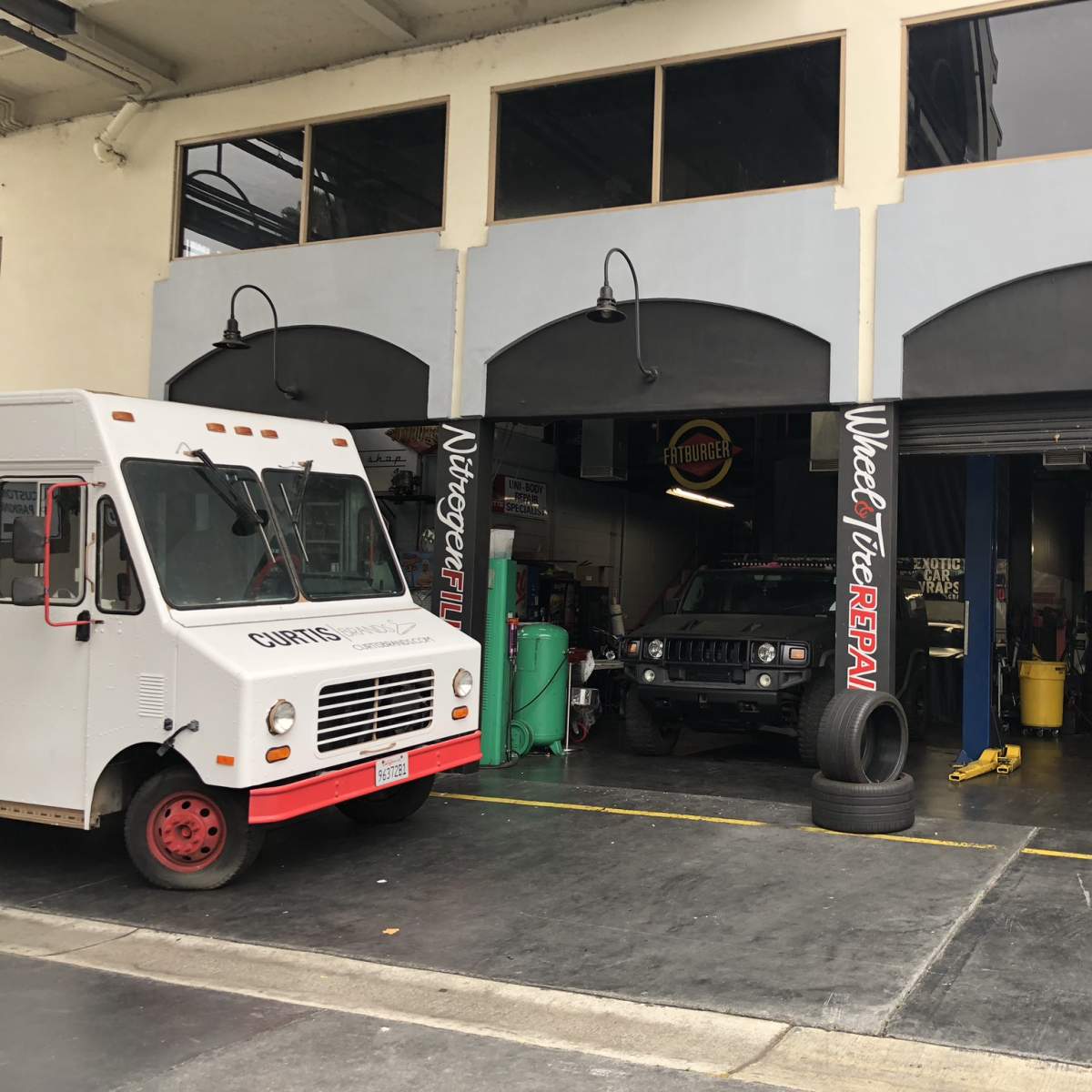 A service garage with two bays, one containing a vehicle and the other featuring a food truck parked outside.