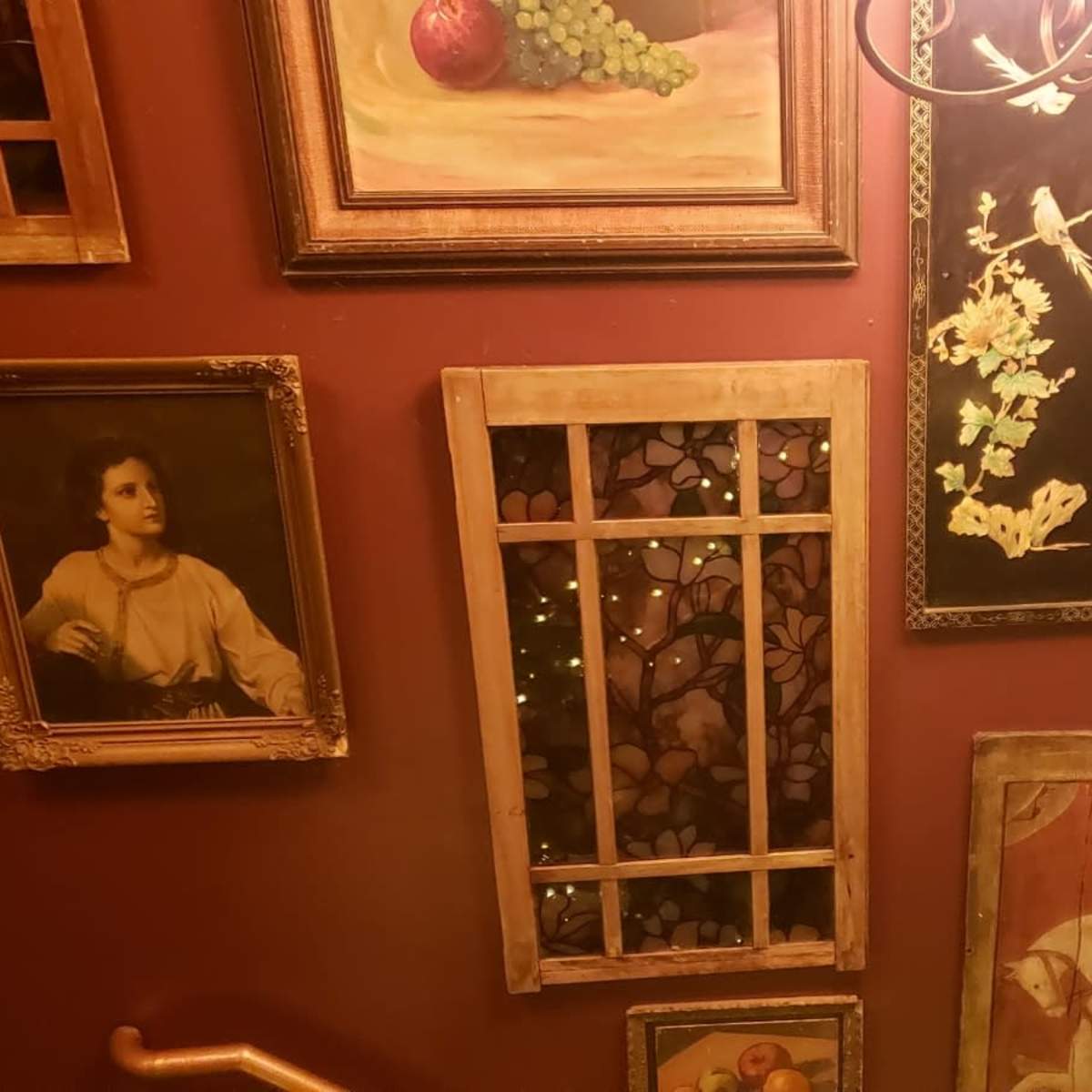 A staircase wall adorned with various framed paintings and decorative elements, illuminated by warm light.