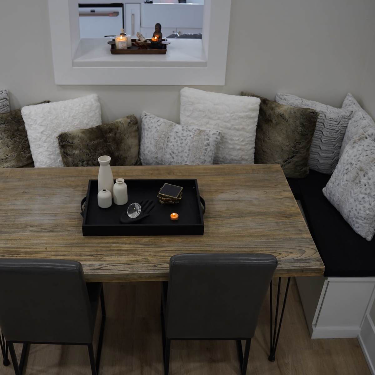 A wooden dining table with a black tray sits in the center of a cozy nook surrounded by plush pillows.