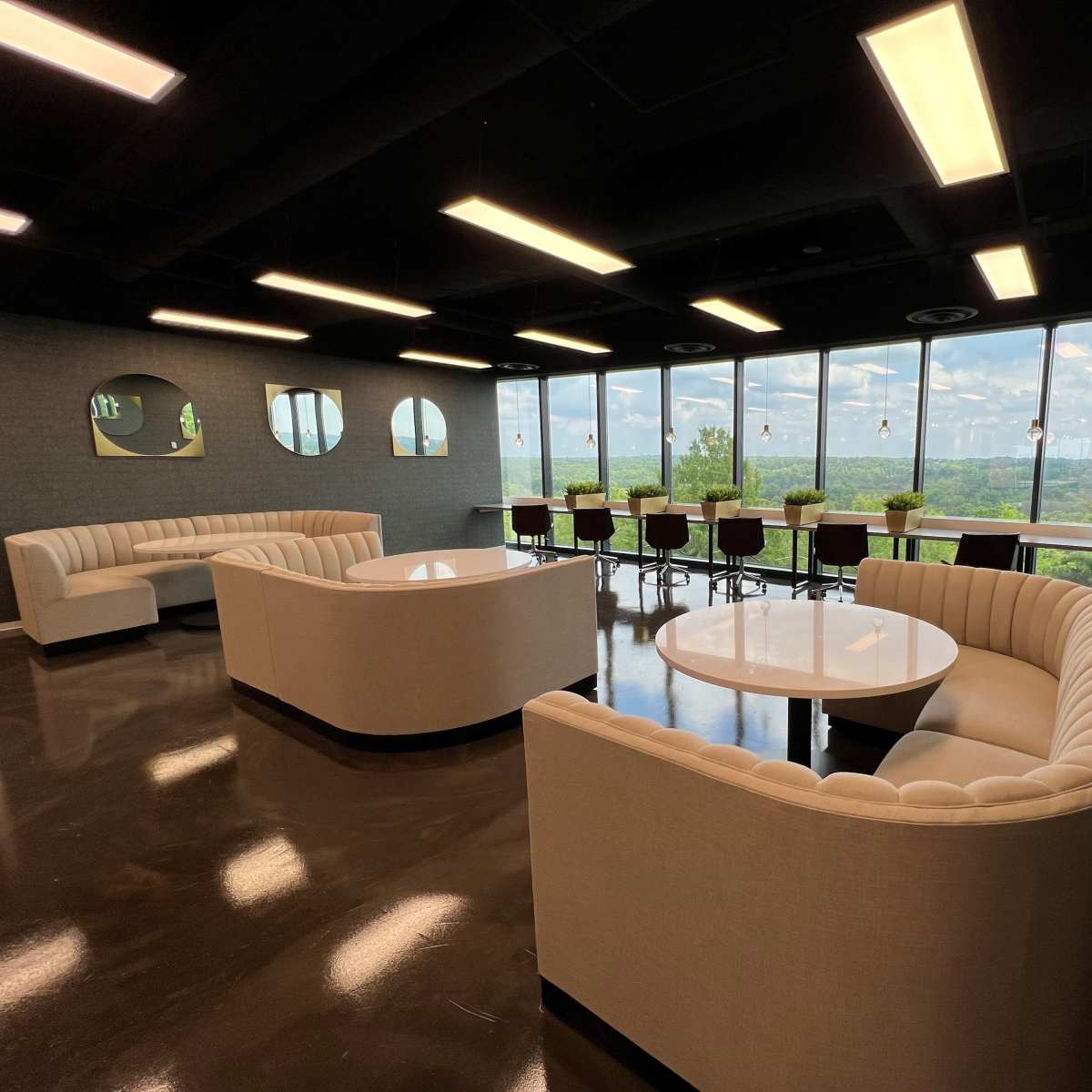 A modern lounge area with curved white seating and round tables near large windows overlooking a scenic view.