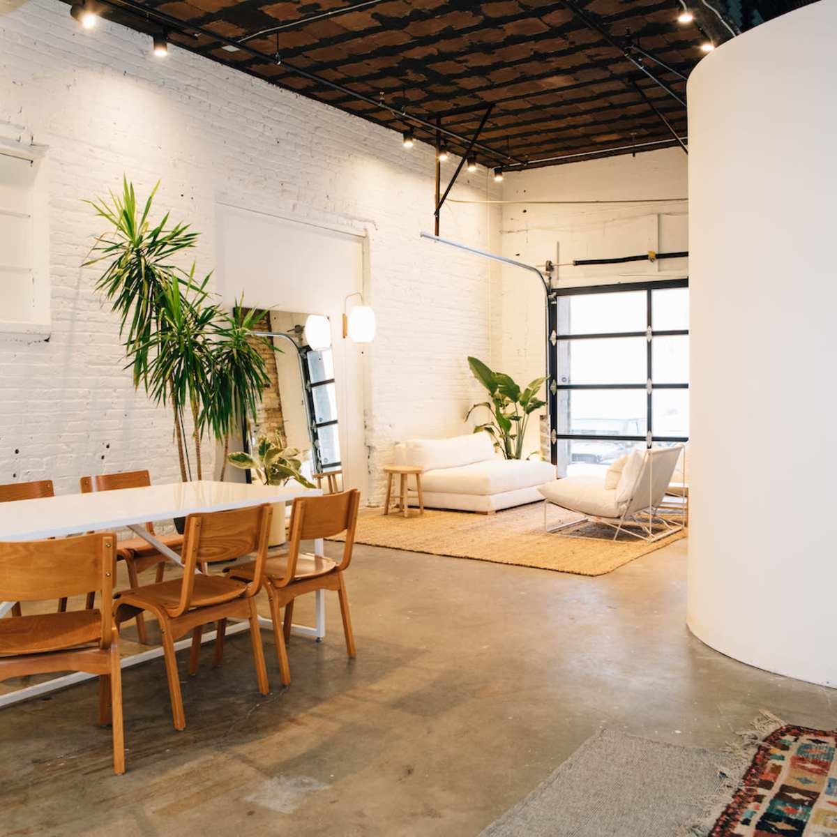 A spacious, modern interior featuring a dining area with a table and chairs, a living space with a sofa, and a large window.