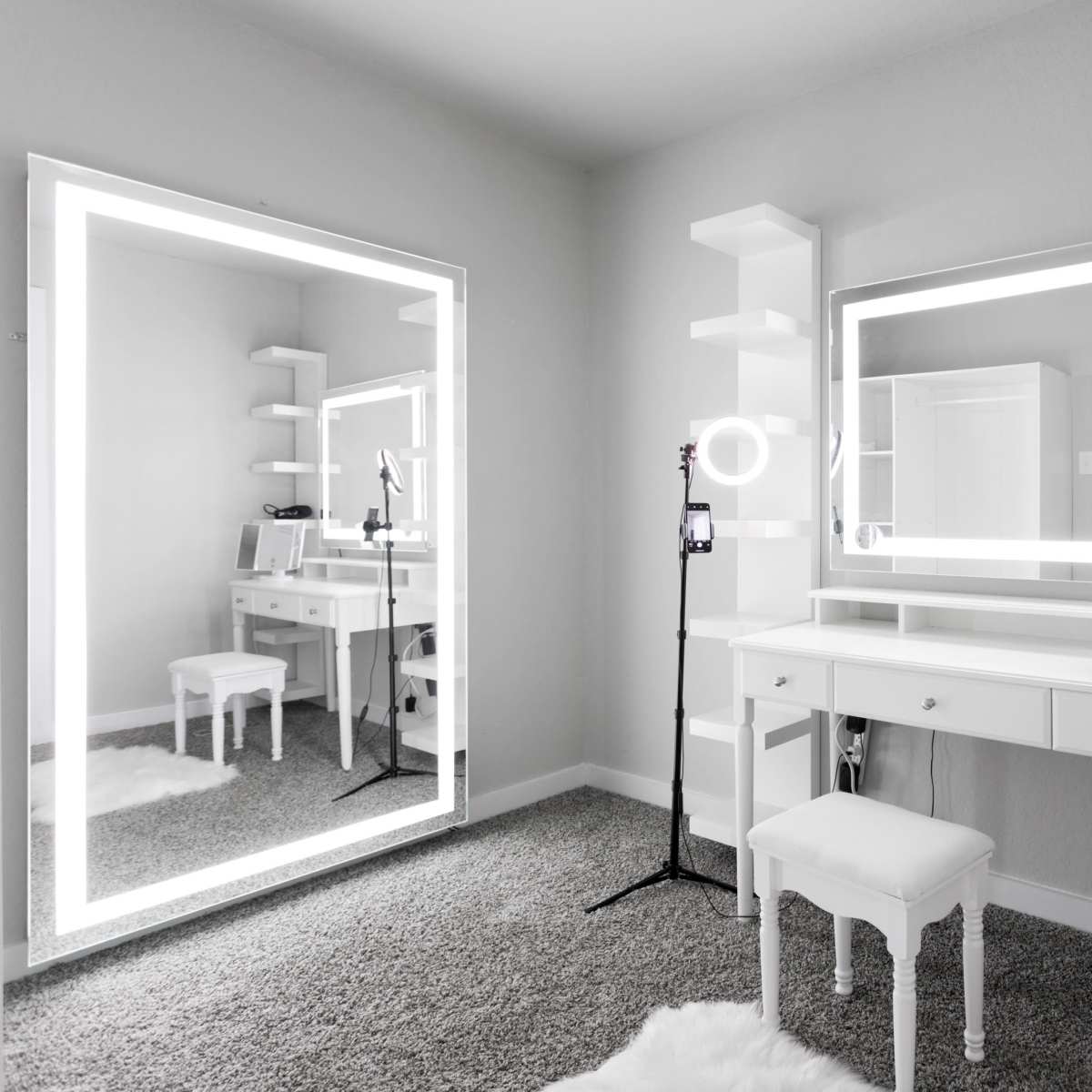 A well-lit vanity area features a white desk with a mirror and shelves, surrounded by gray carpet.