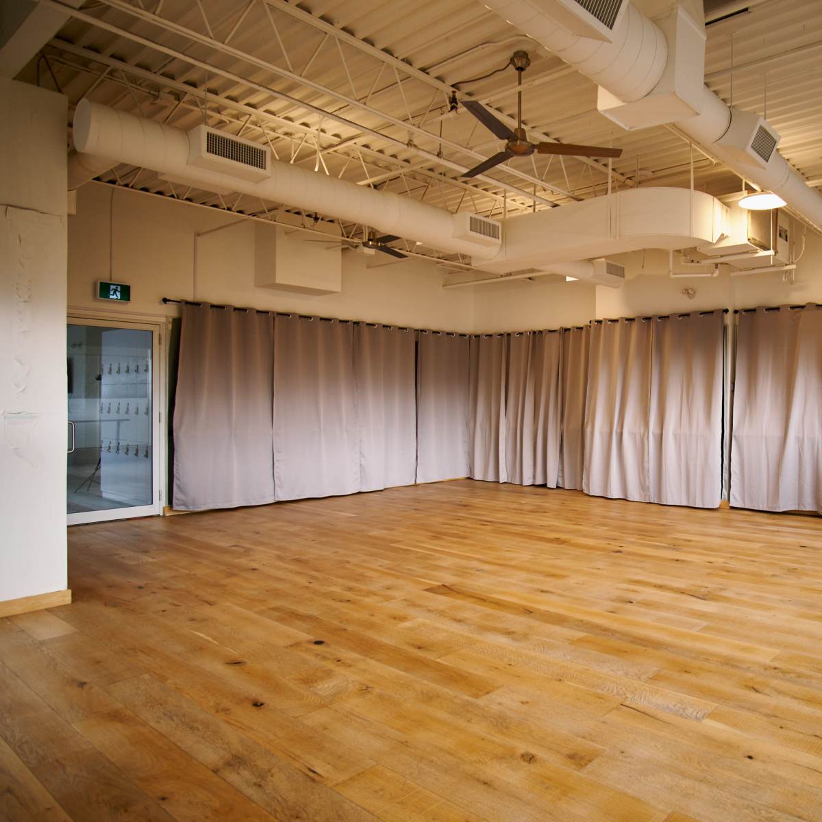 An empty dance studio featuring wooden flooring and gray curtains along the walls.