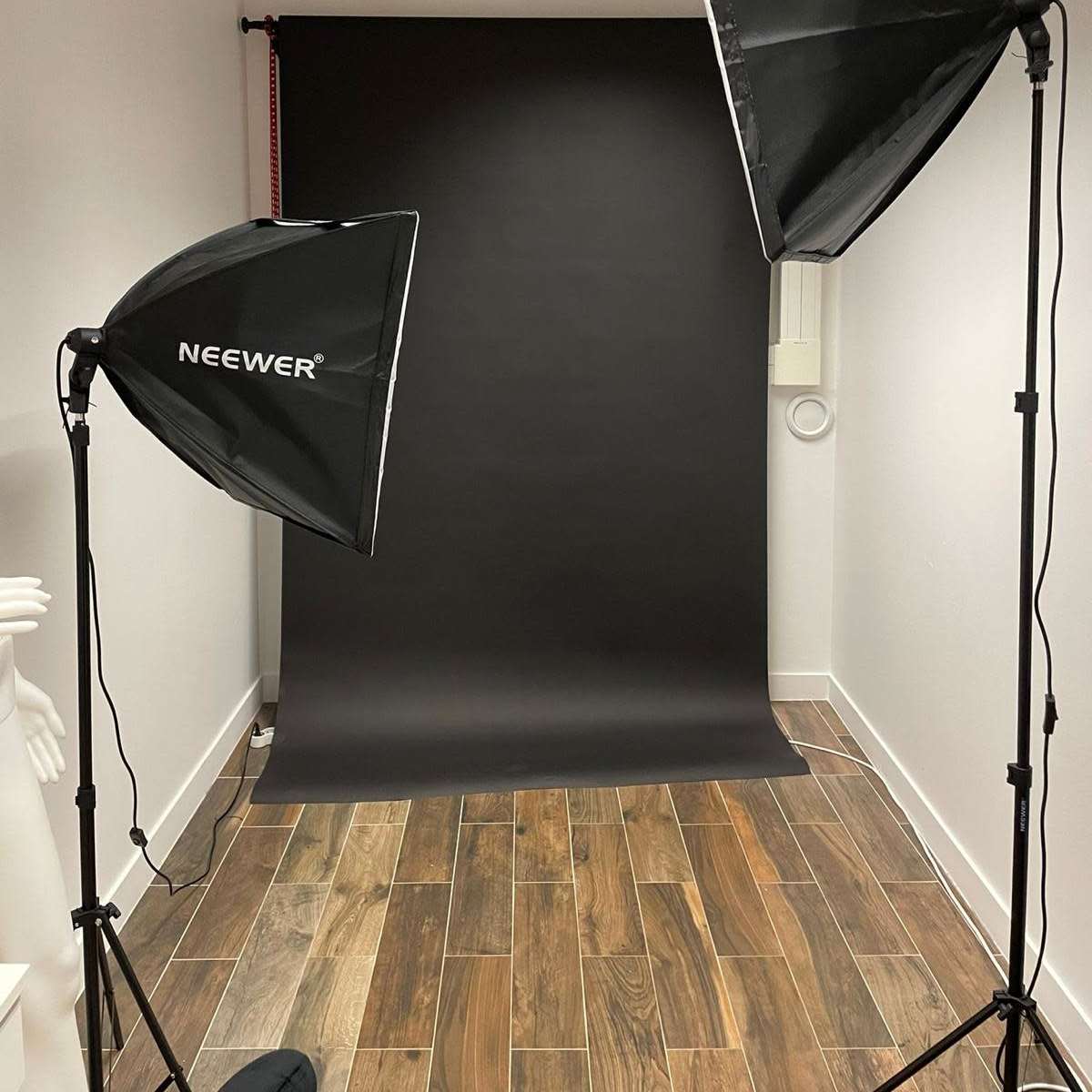 A photography setup with two softbox lights positioned on either side of a black backdrop in a room with wooden flooring.