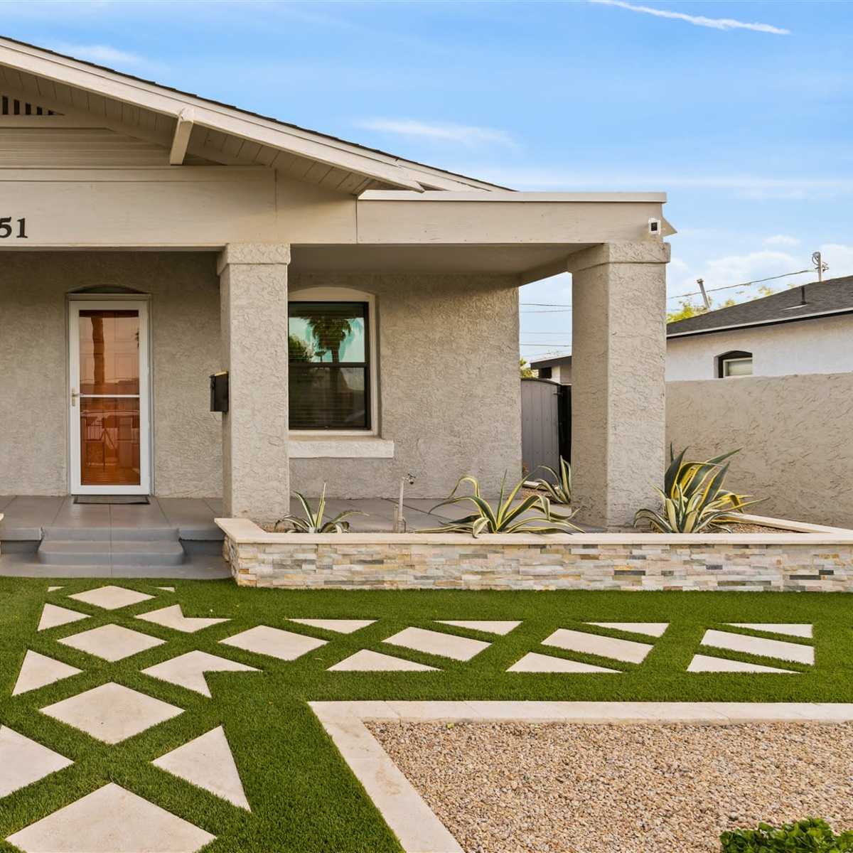A modern single-story house with a stone-accented facade, manicured lawn, and geometric pathway leading to the front door.