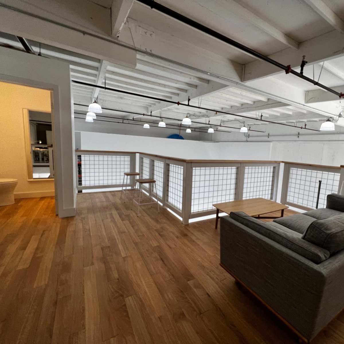 A spacious, well-lit room with wooden flooring, a gray couch, and a railing overlooking an open area.