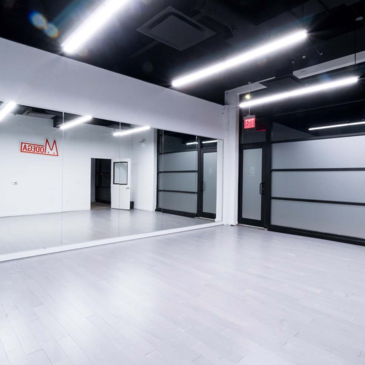 A spacious, well-lit room featuring mirrored walls and a glass door.