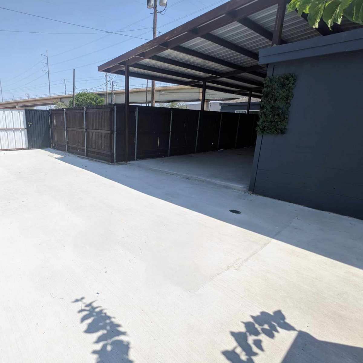 A paved, empty outdoor space enclosed by wooden fences and a building with a metal roof.