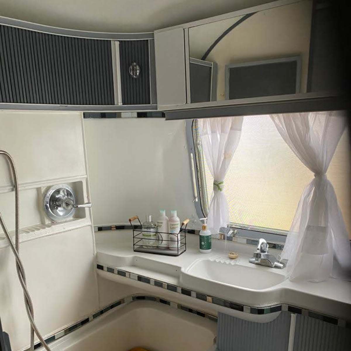 A compact bathroom featuring a wooden slatted bathtub, sink area with various toiletries, and a showerhead attached to the wall.
