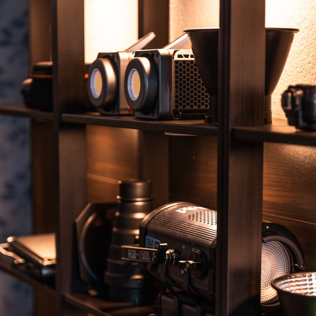A wooden shelf displaying various photography equipment, including cameras, lighting devices, and accessories organized neatly.