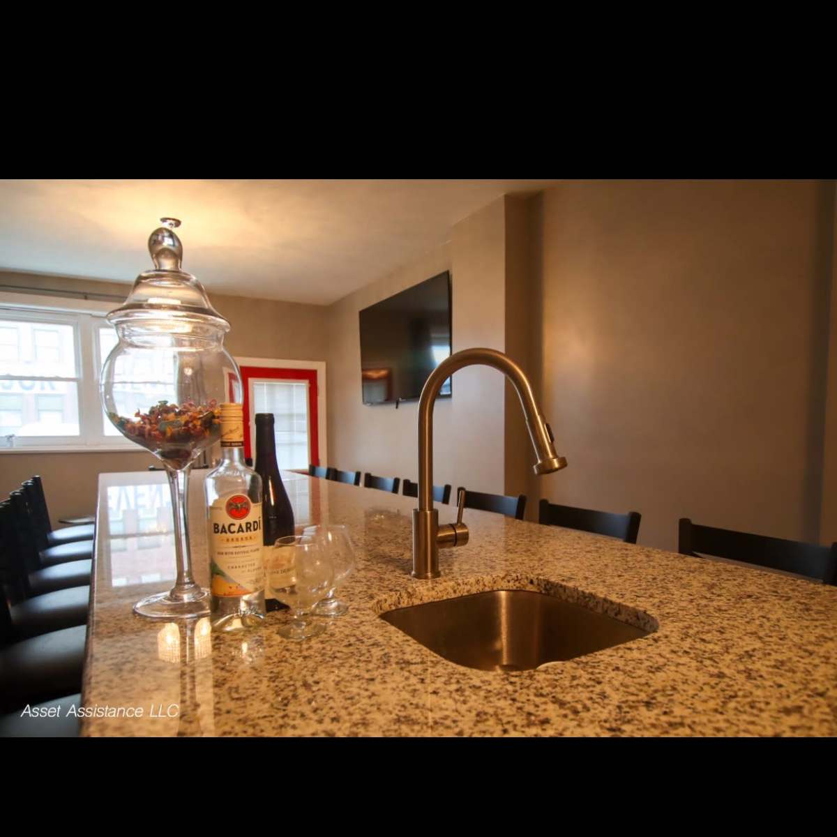 A modern kitchen with a granite countertop, a stainless steel sink, a bottle of liquor, and a glass jar filled with various items.