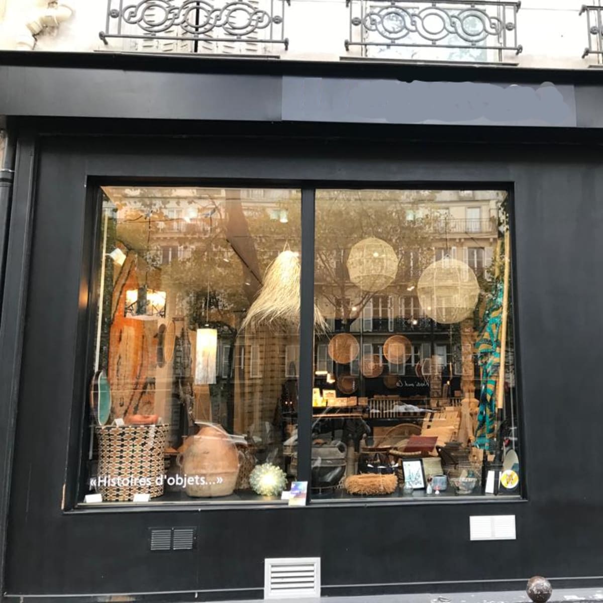 A black storefront displays a large window filled with various decorative items and furniture.