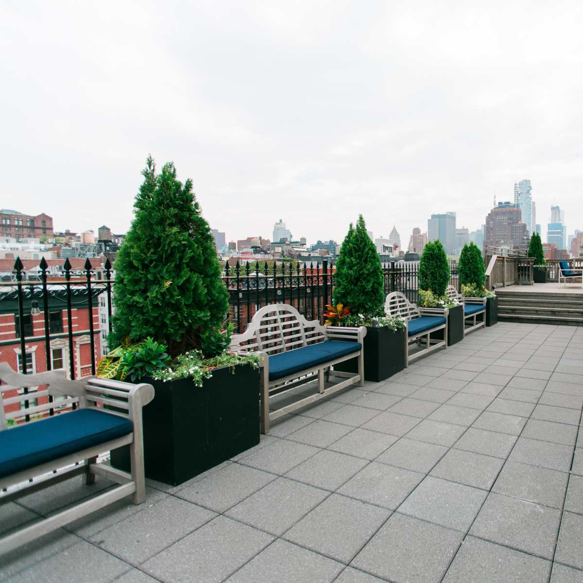 A rooftop terrace with neatly arranged benches, planters, and city skyline views in the background.