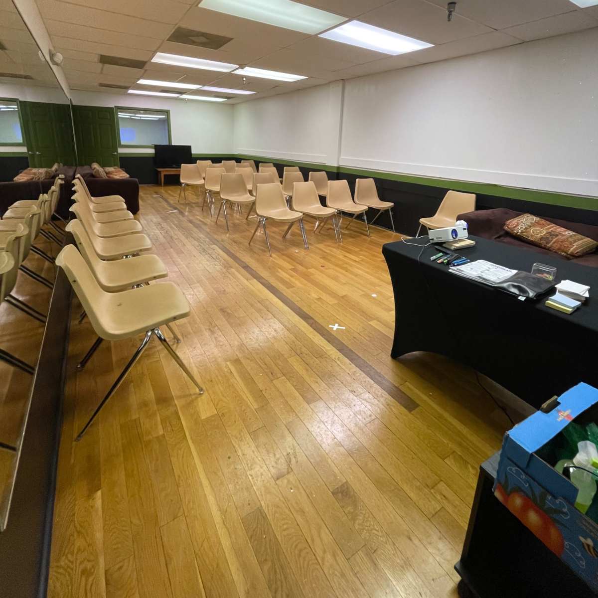 A sparsely furnished room with rows of empty chairs and a table at the side, featuring a roll of paper and a box.