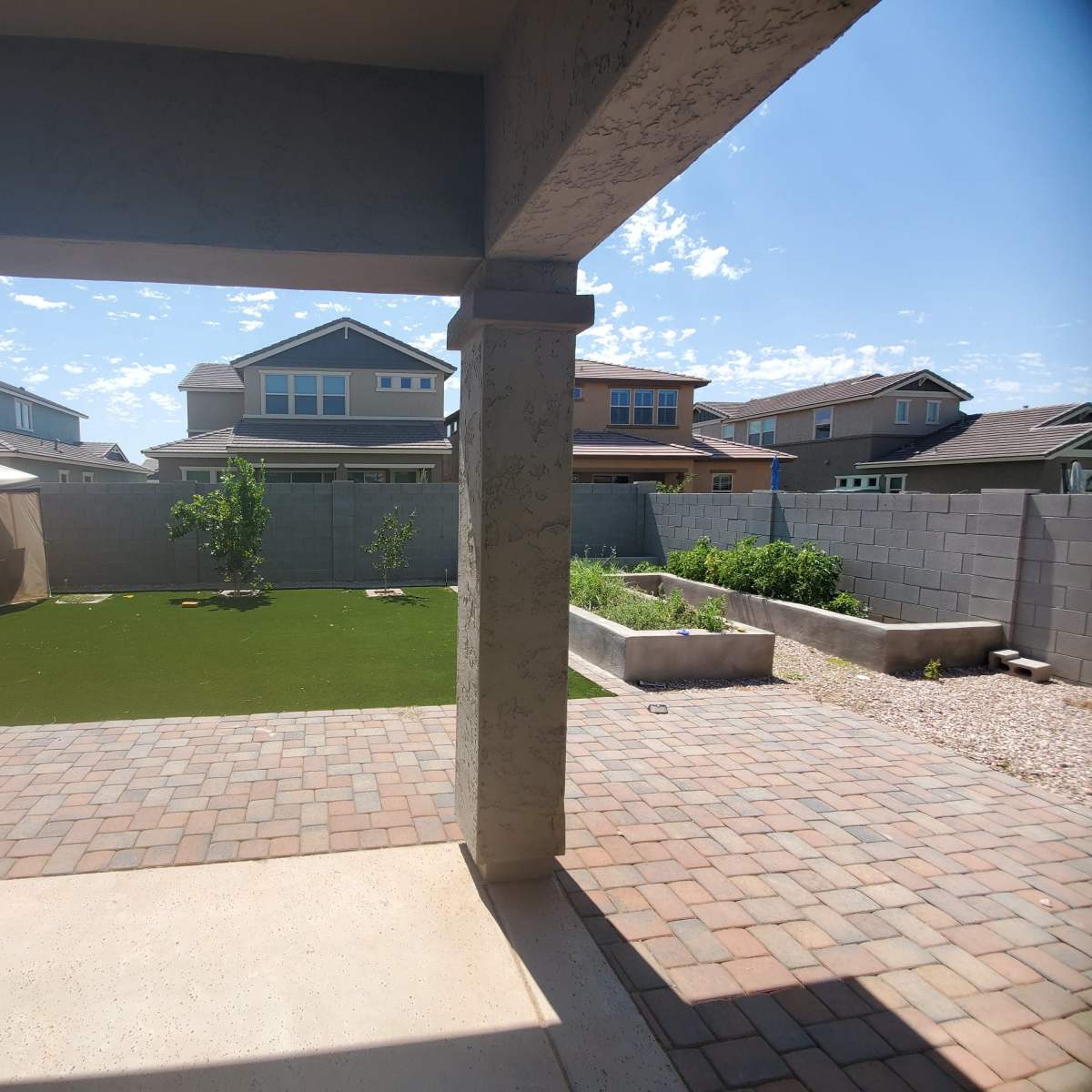 A backyard view featuring a manicured lawn, garden beds, and a gazebo, framed by a concrete patio and surrounding houses.