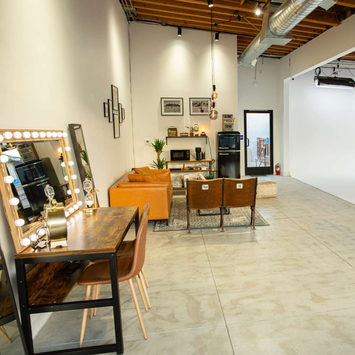 A spacious studio with a white backdrop, a seating area featuring a leather sofa and chairs, and a mirrored vanity table against one wall.
