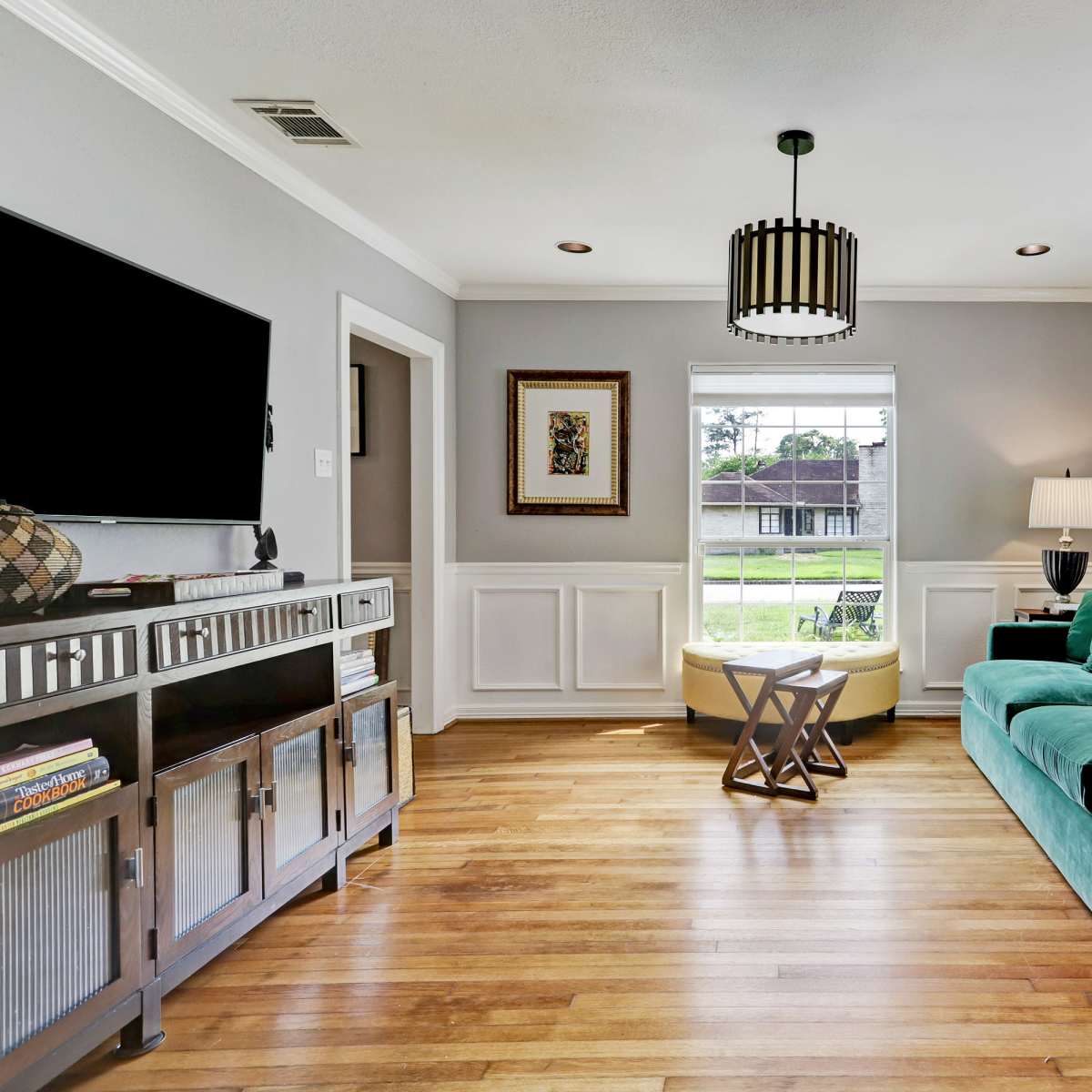 The living room features a green sofa, a television mounted on the wall, and a window with a view of the outdoors.