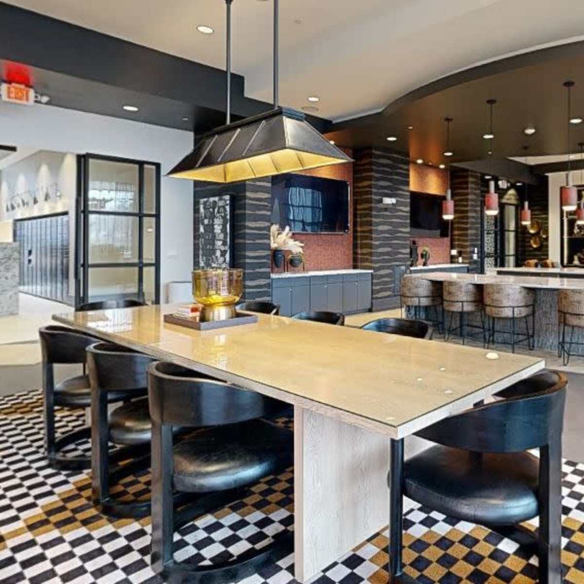 A modern lounge area featuring a large table with black chairs, a kitchen bar with stools, and a decorative fireplace in an open space.