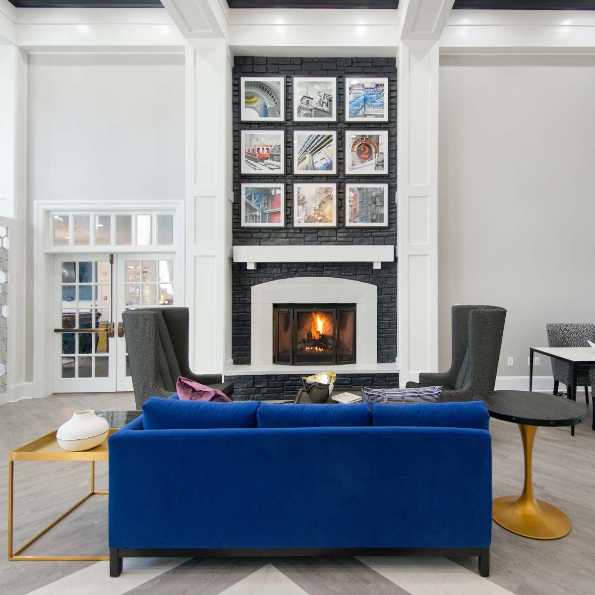A modern living room features a blue sofa, a gold side table, a fireplace surrounded by a black stone mantle, and framed artwork on the wall.