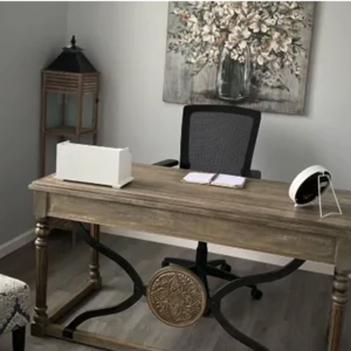 A minimalist office space featuring a wooden desk, a black office chair, and a floral wall art.
