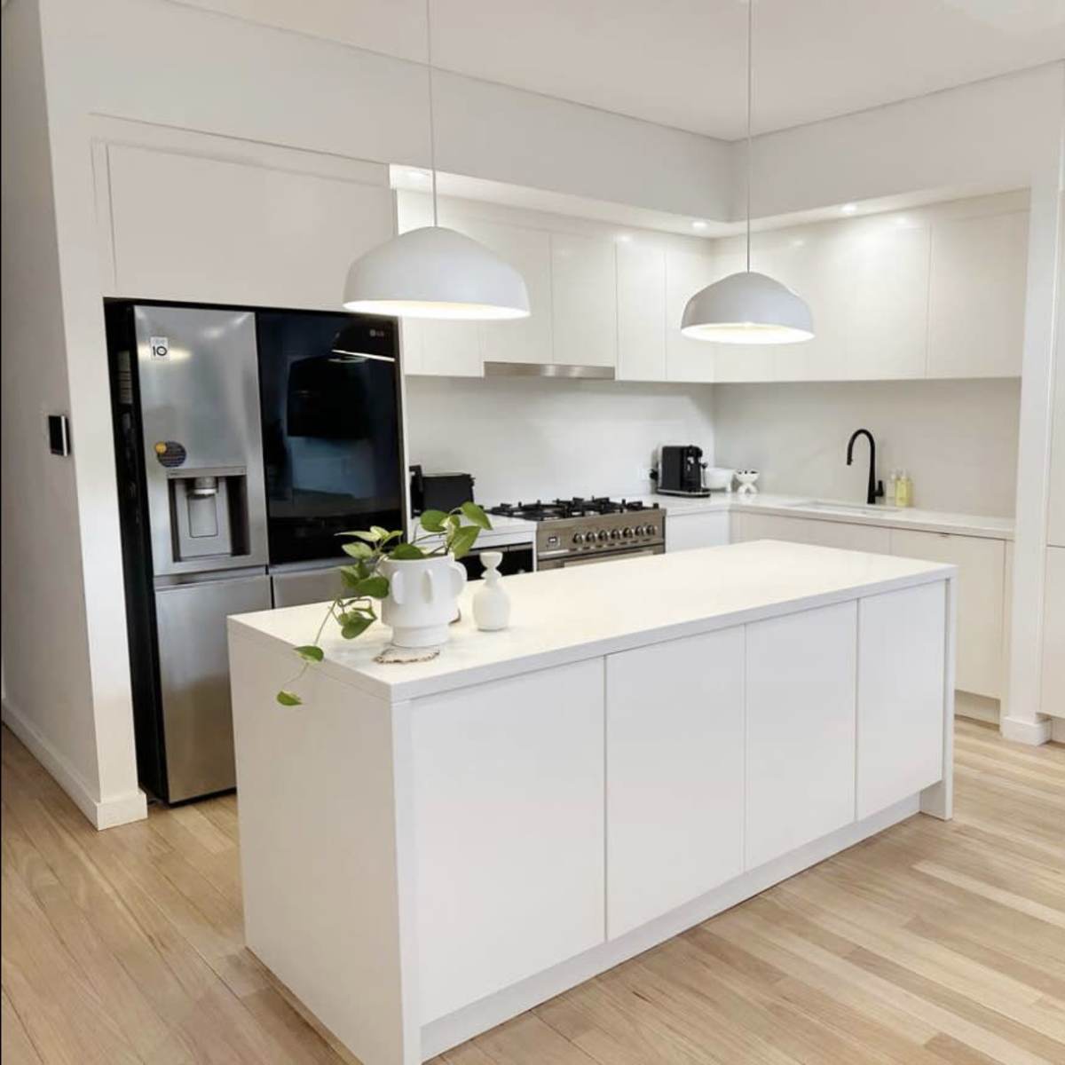A bright, modern kitchen features a central island with a white countertop, white cabinets, a black refrigerator, and pendant lighting.