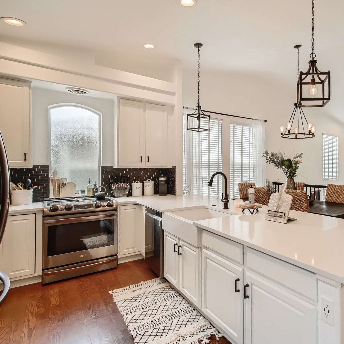 A modern kitchen features a central island with a sink, surrounded by white cabinetry, and is connected to a dining area illuminated by pendant lights.