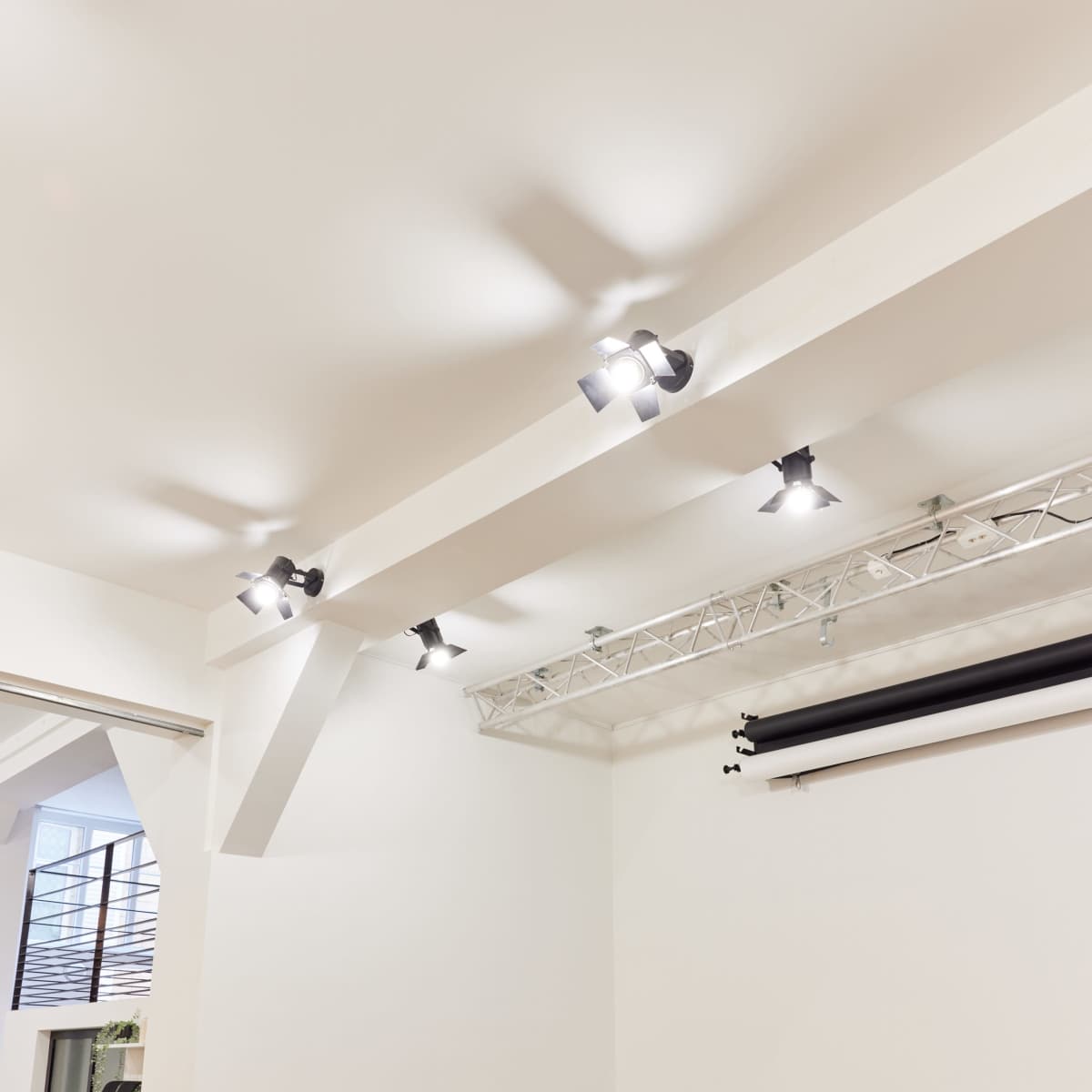 A minimalist studio space with a white wall, track lighting, and two wooden chairs.