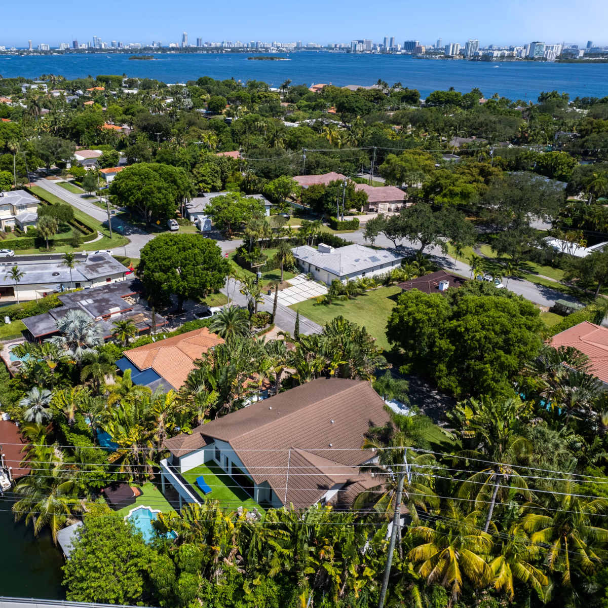 A coastal neighborhood with homes and boats lining a canal, set against a backdrop of a city skyline and blue water.