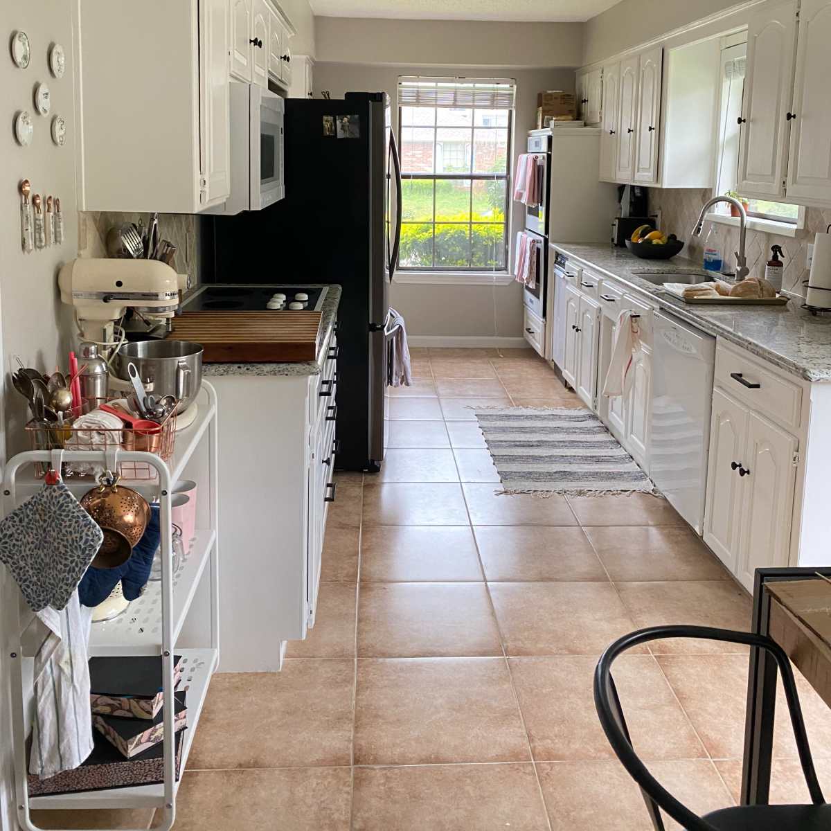 A tidy kitchen features white cabinets, a black refrigerator, and a window overlooking a green outdoor space.