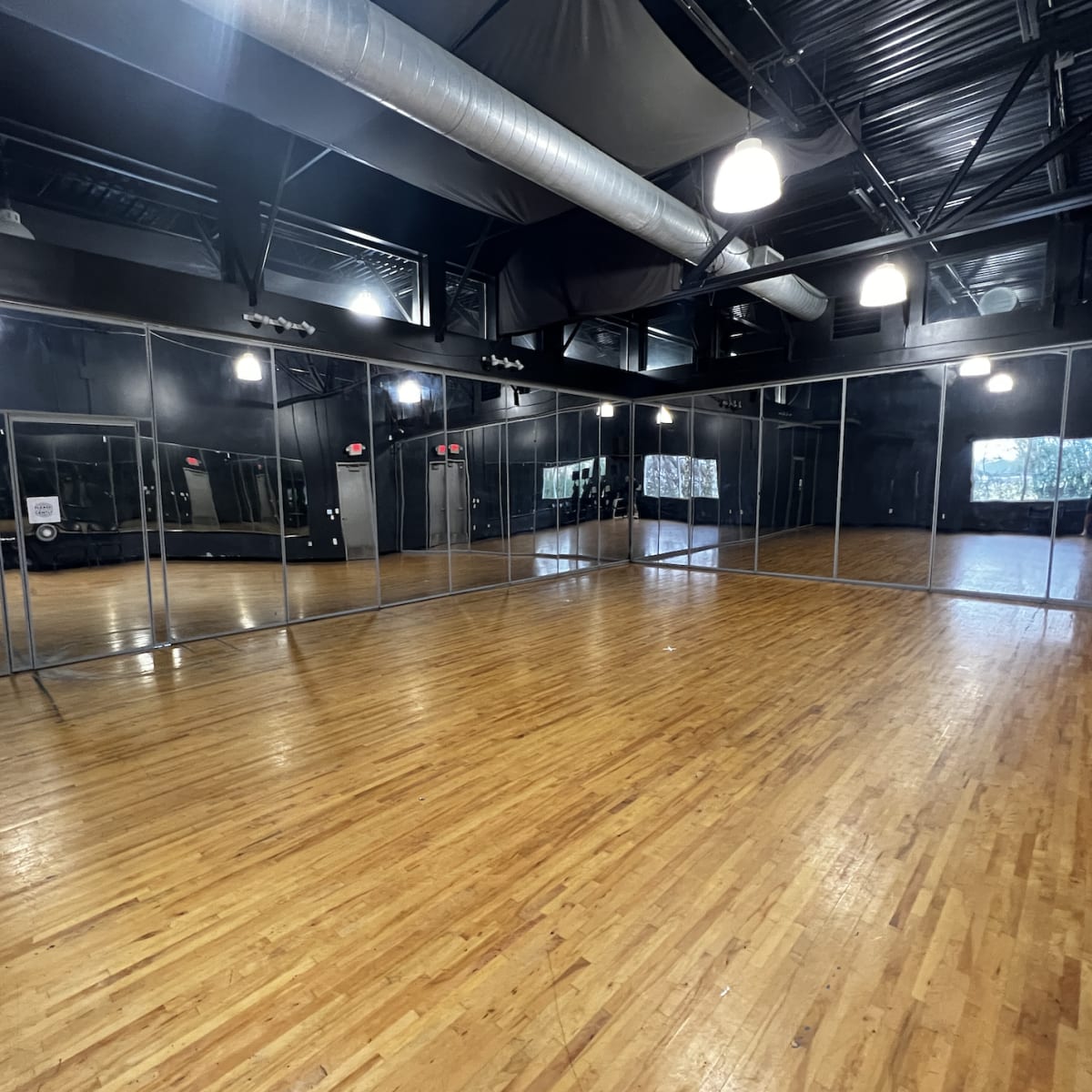 A large, empty dance studio with wooden flooring and mirrored walls.