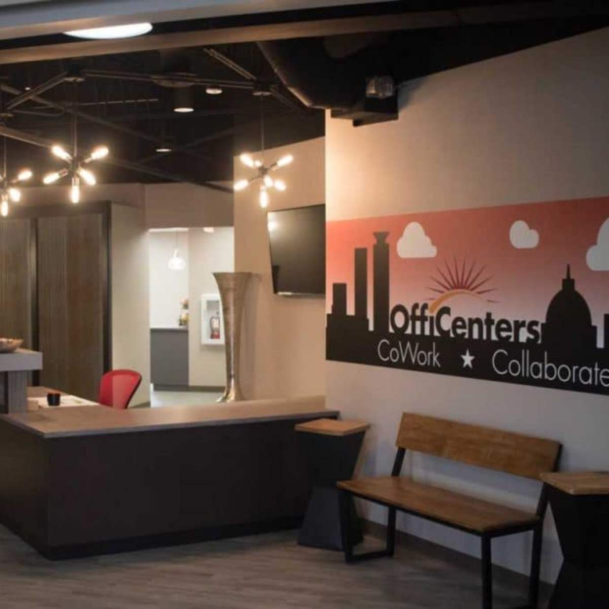 A modern coworking space featuring a reception area with seating, decorative lighting, and branding on the wall.