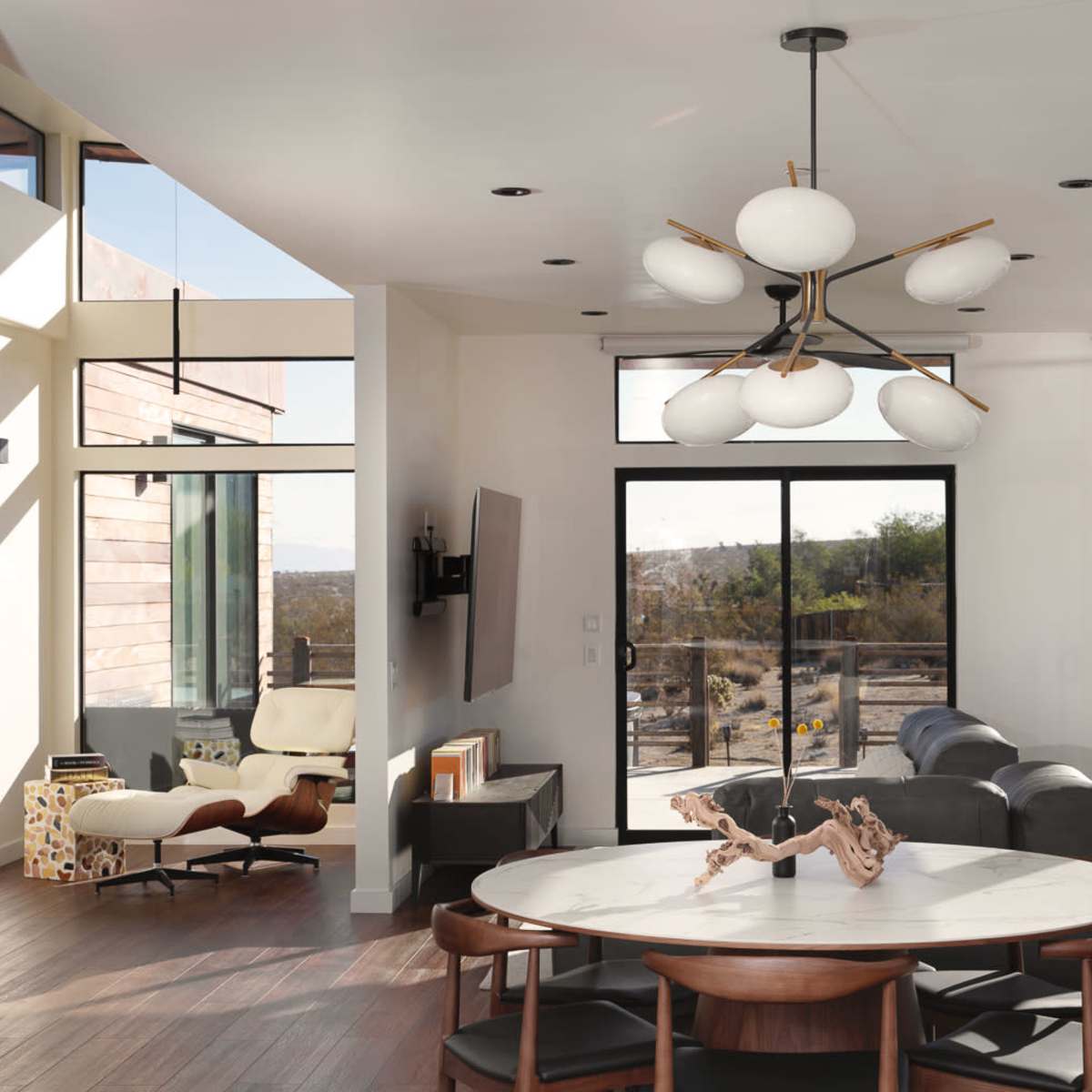 A modern living room with large windows, a round dining table, and a stylish light fixture.