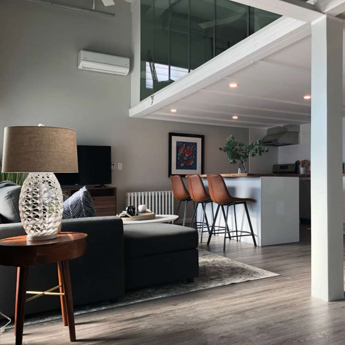 A modern open-concept living area with a kitchen island, bar stools, a sofa, and a television.