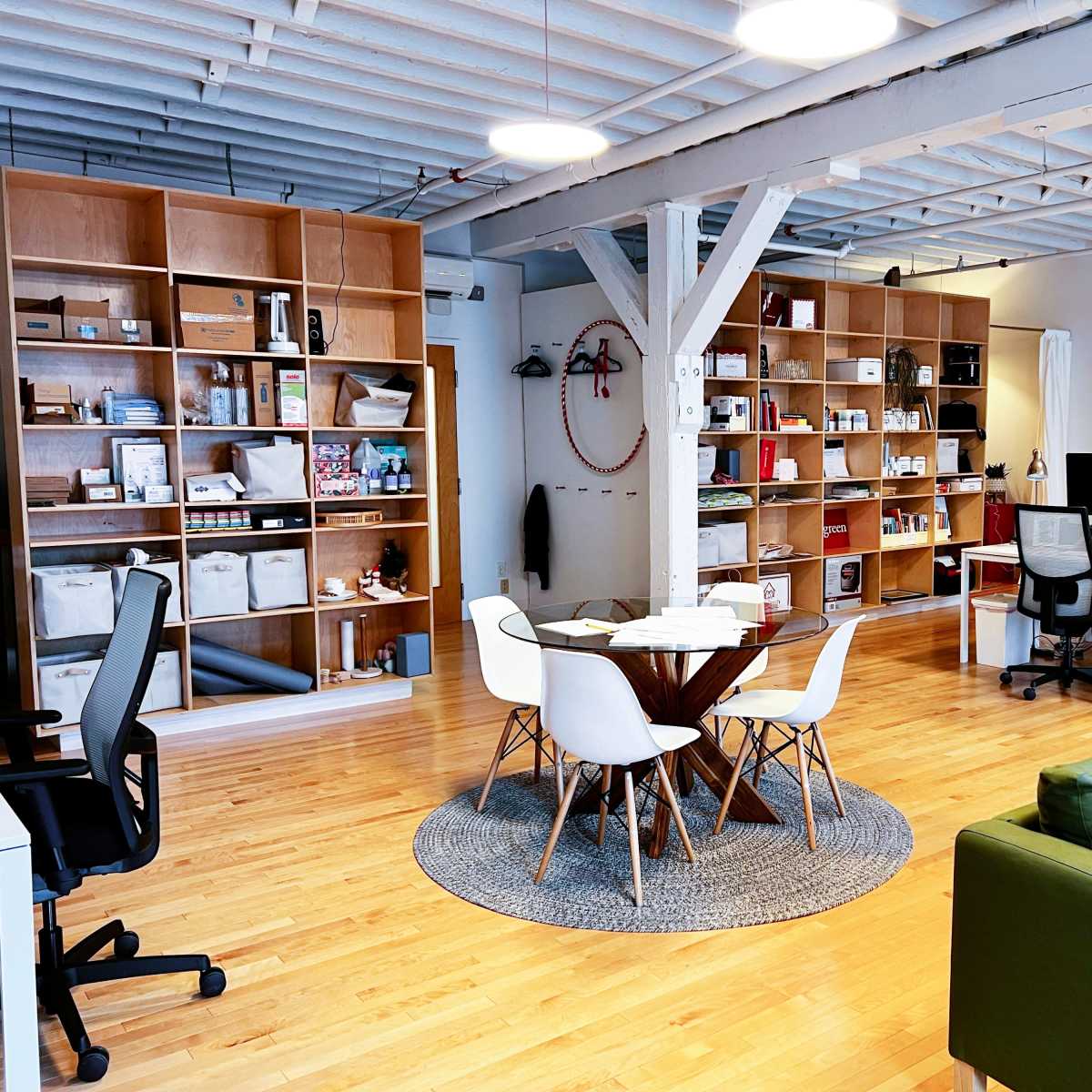 A modern open-office space featuring a round table with chairs, a green couch, and wooden shelves filled with various items.