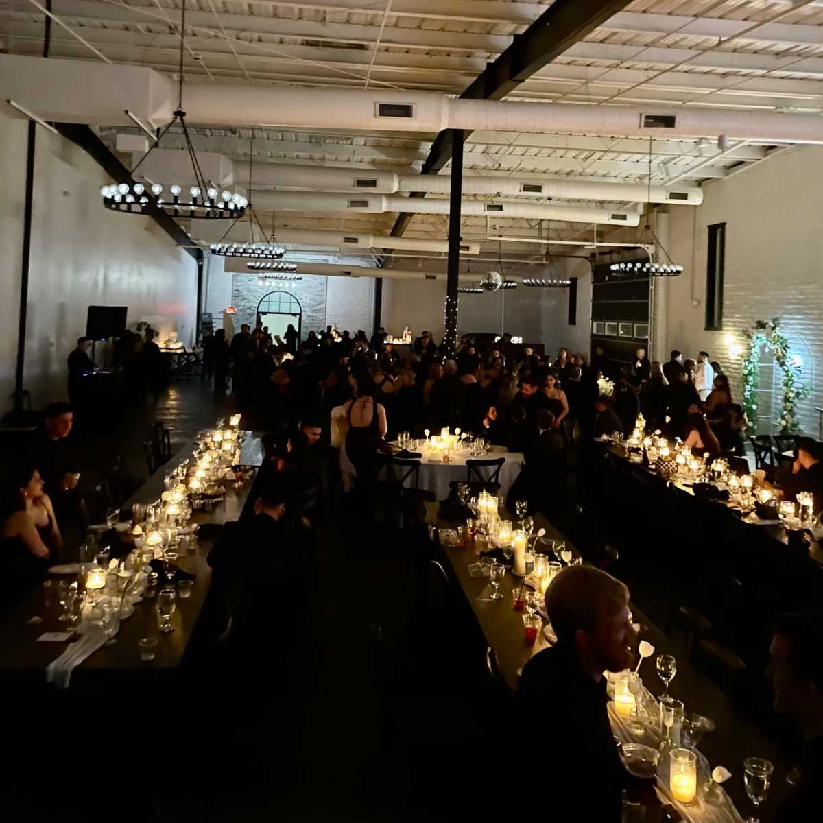 A large indoor venue is filled with guests seated at tables adorned with candles during an evening event.