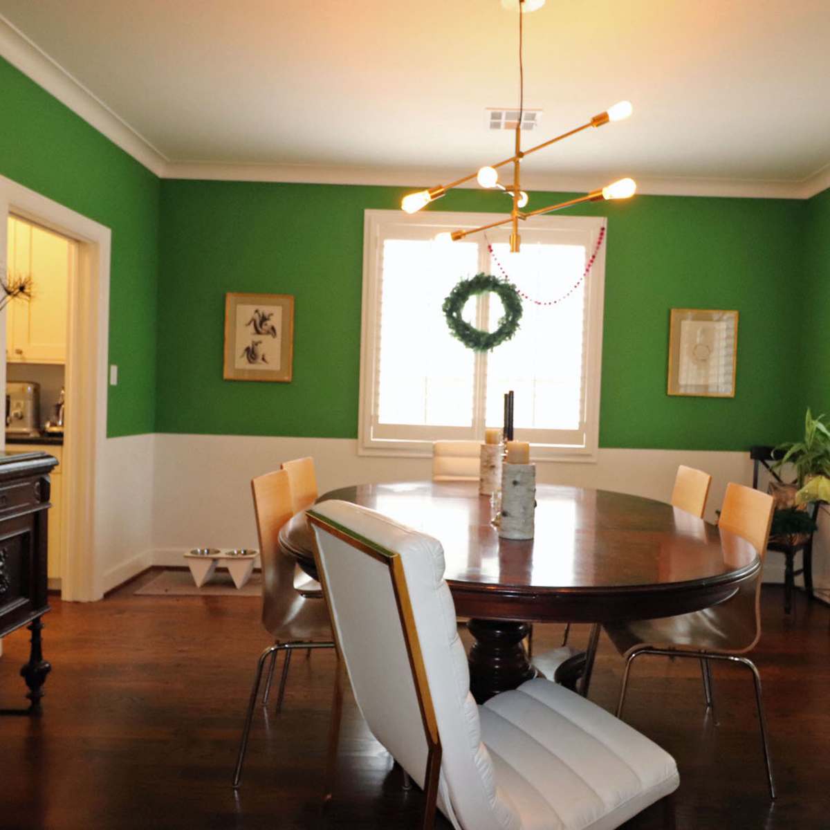 The dining room features a round wooden table surrounded by modern chairs, with green walls and festive decorations.