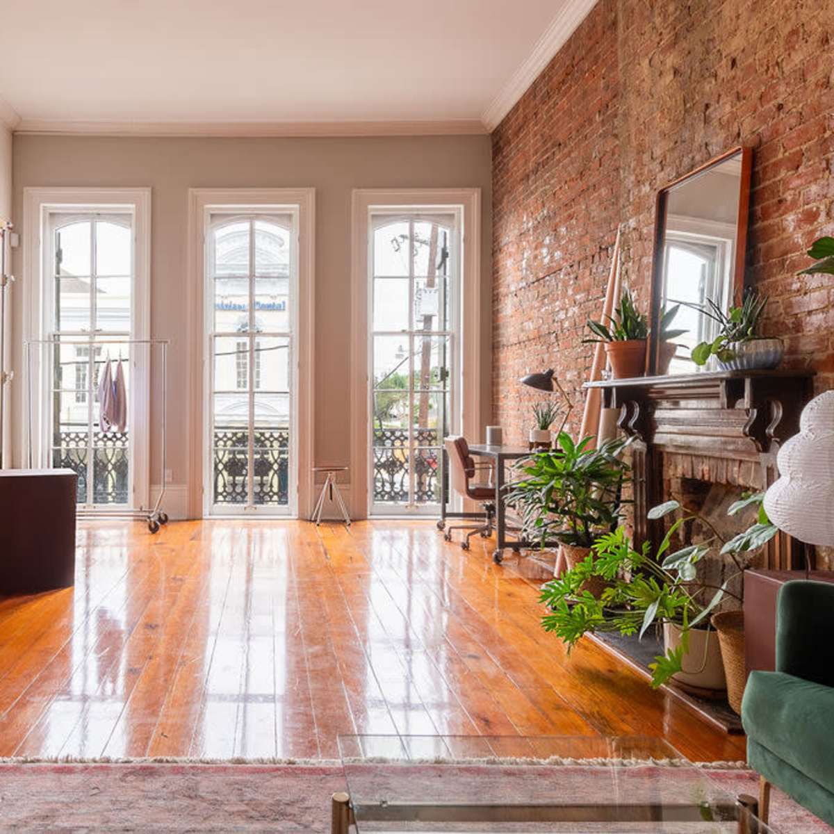 A spacious room with large windows, hardwood floors, a brick wall, a backdrop stand, and a mirror.