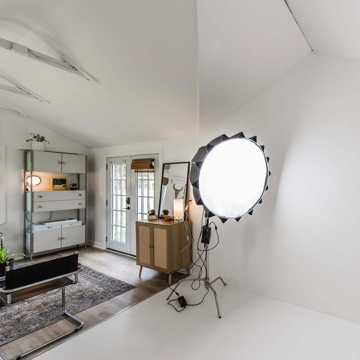 A bright, minimalistic studio space featuring a circular softbox light and a neutral-colored wall.