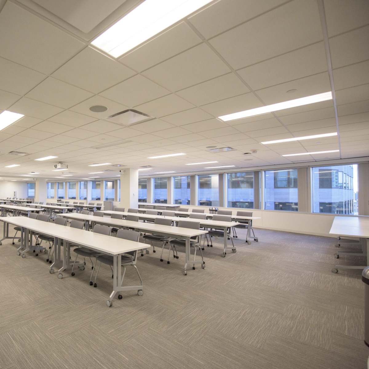 A spacious, well-lit conference room with multiple tables arranged in rows and large windows providing natural light.