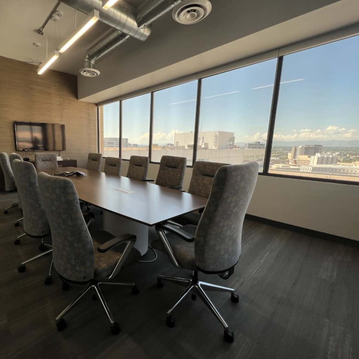 A modern conference room features a large table surrounded by ten ergonomic chairs, with floor-to-ceiling windows showcasing a city view.