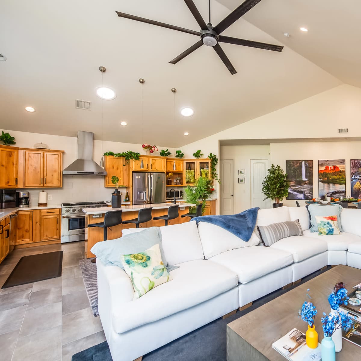 A spacious living area featuring a large sectional sofa, a coffee table with magazines, and a kitchen with wooden cabinetry and a ventilation hood.