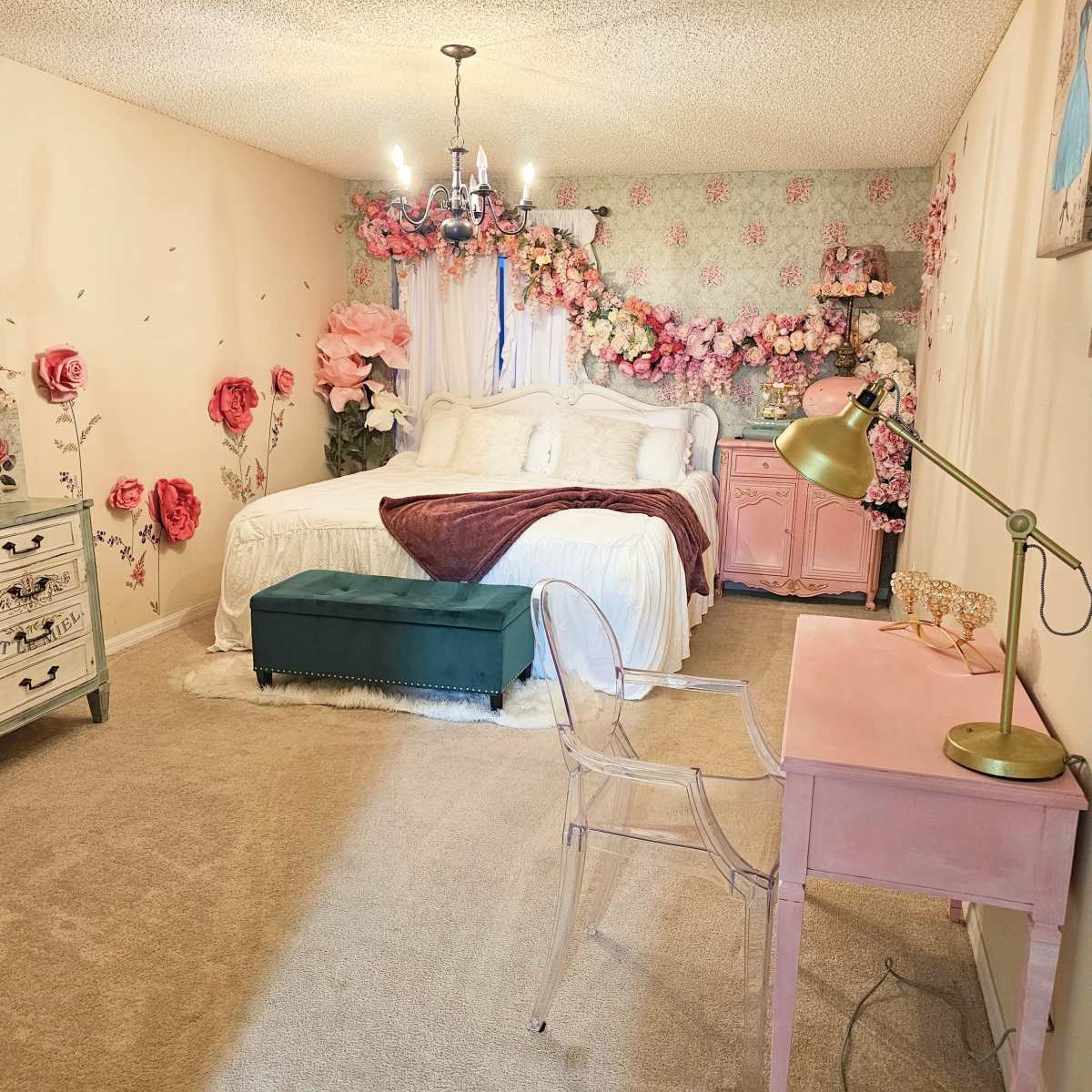 A decorated bedroom with a bed, floral accents on the walls, a small desk with a lamp, and a green ottoman.