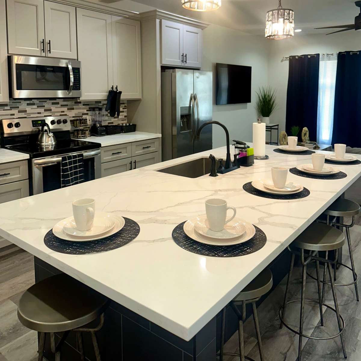 A modern kitchen features an island with place settings and pendant lights, alongside stainless steel appliances and gray cabinetry.